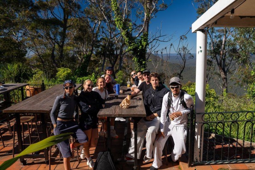 A group of people sitting at an outdoor table with a scenic view of trees and hills in the background. 3