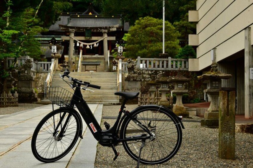 A black bicycle parked on a paved path with a traditional Japanese building in the background. 2