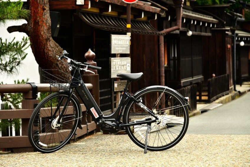 A black bicycle parked on a gravel path next to a traditional wooden building with a sign. 1