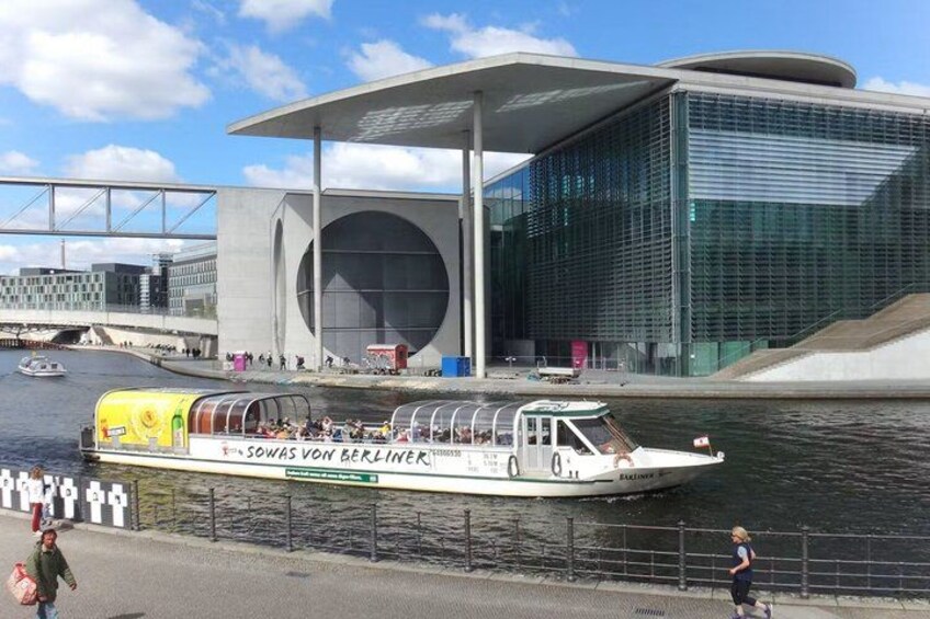 A riverboat with 'Sowas Von Berlin' written on it, docked near a modern building with a large circular window. 4