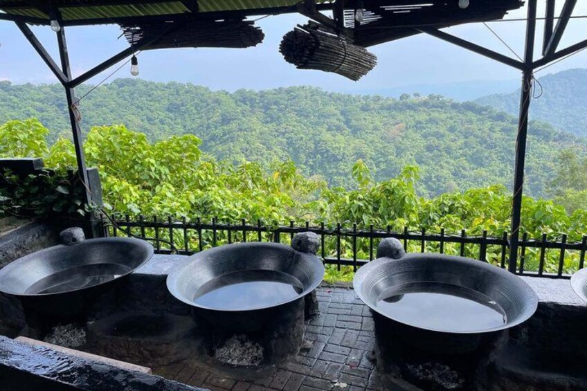 Outdoor cooking pots on a brick platform with a view of a lush green forest. 4
