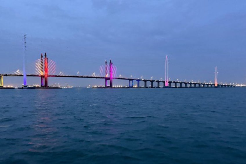 A long bridge with multiple towers, illuminated by colorful lights, spanning across a body of water. 3