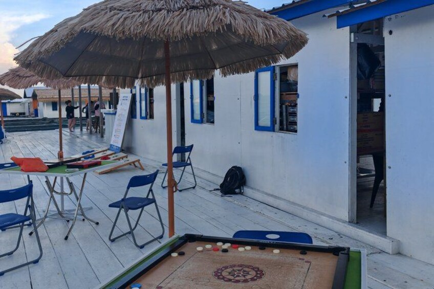 A pool table with chairs and a thatched umbrella on a wooden deck. 5