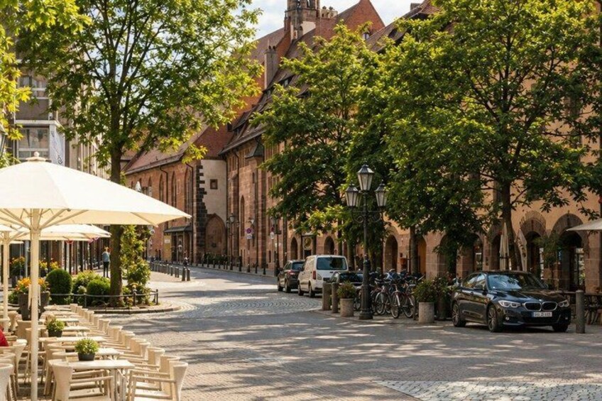 A cobblestone street lined with trees and buildings, a café with outdoor seating, and parked cars. 5