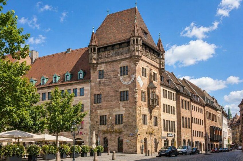 A historic building with a steep roof and arched windows, surrounded by trees and parked cars. 2
