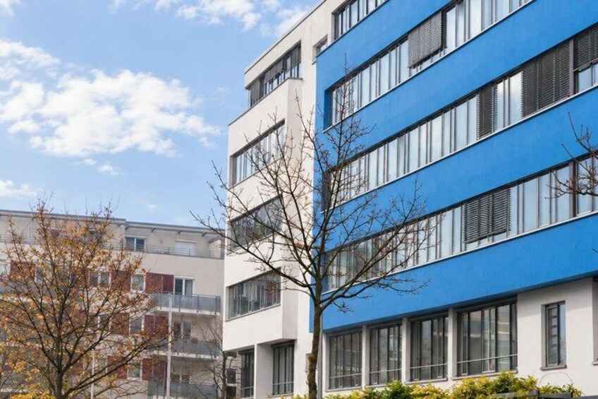 A modern building with blue and white exterior walls, multiple windows, and a tree in the foreground. 5