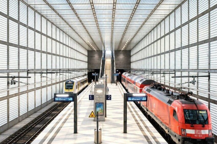A modern train station with two trains on parallel tracks, overhead signage, and a glass ceiling. 5