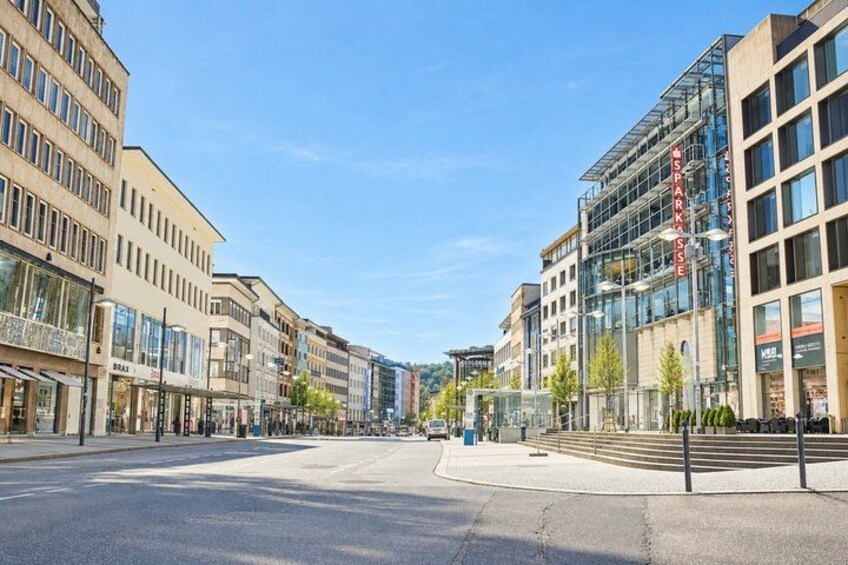 A wide urban street with modern buildings, a clear sky, and a pedestrian crossing. 4