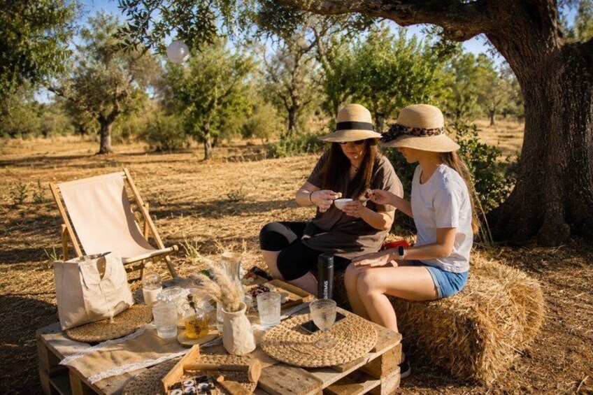 Two people sitting at a picnic table outdoors with a hat, a bottle, and a basket. 1