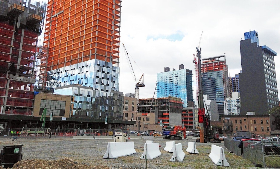 Un sitio de construcción con varios edificios en proceso de construcción, incluyendo un edificio alto de color naranja y uno de vidrio azul. 2