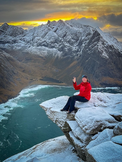 A person sitting on a snow-covered rock by a river with mountains in the background. 2