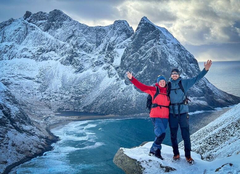 A couple on a snowy mountain peak with a fjord and a stormy sky in the background. 1