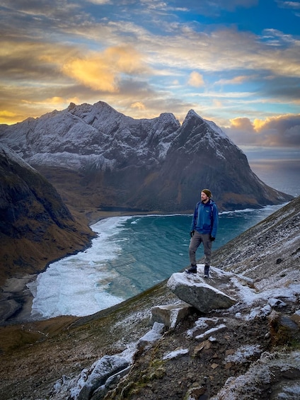 A person standing on a rocky outcrop overlooking a glacier and mountains. 5