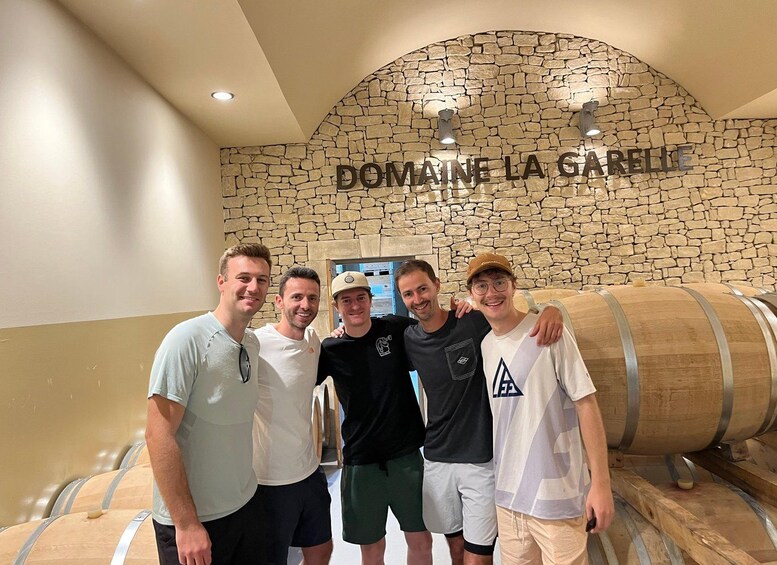 A group of people standing in front of a stone wall with the text 'DOMAINE LA GARELLE' and wooden barrels. 2