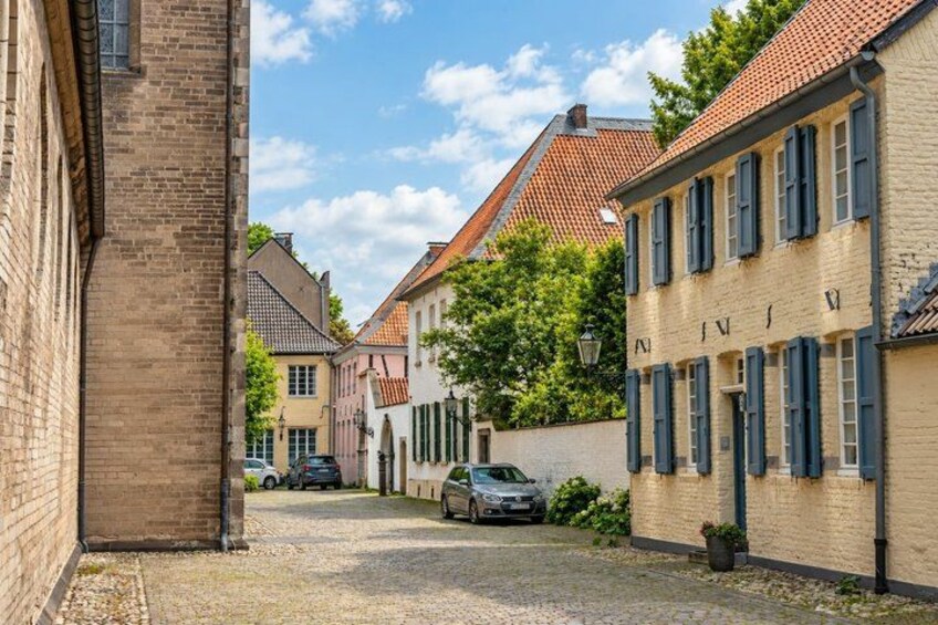 A cobblestone street lined with historic buildings, a parked car, and a clear sky. 3