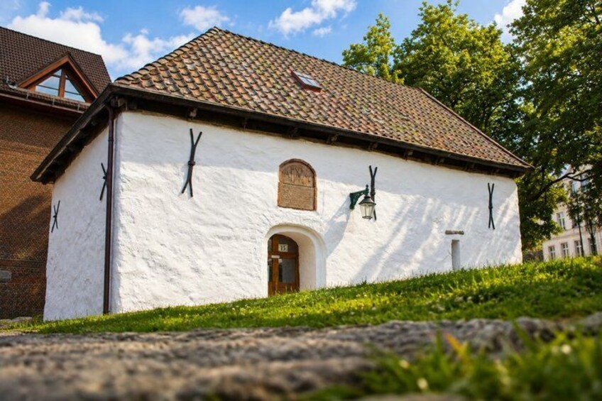 A white building with a brown roof, a wooden door, and black clock faces on the walls. 5