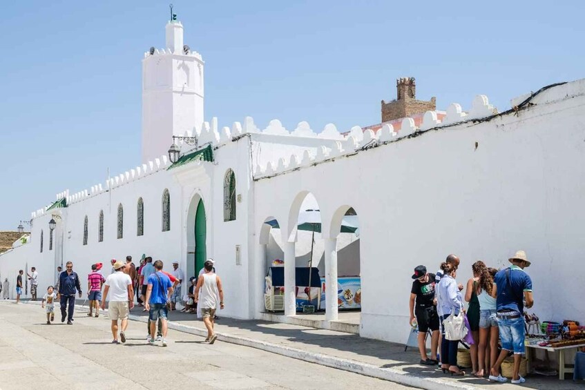 Ein weißes Gebäude mit Bögen und einem Minarett, umgeben von Menschen. 2