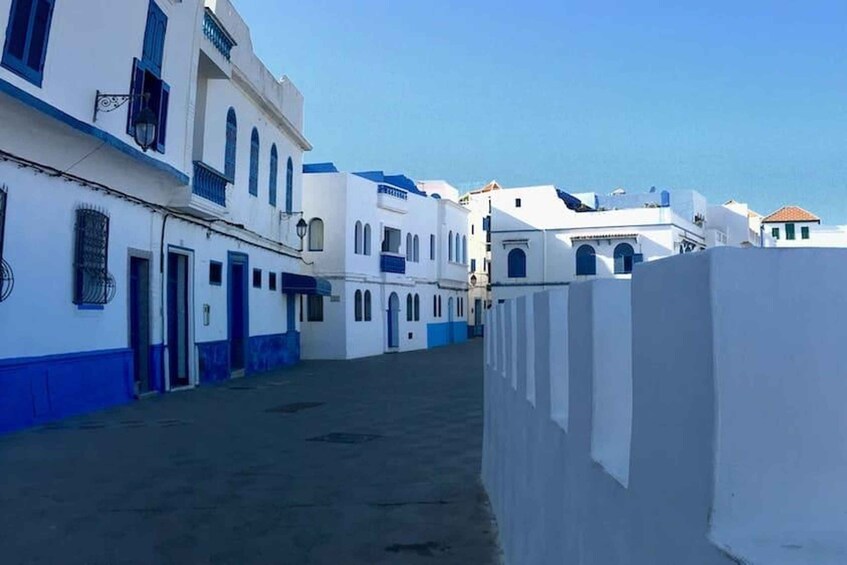 Eine schmale Straße gesäumt von weißen Gebäuden mit blauen Akzenten, unter blauem Himmel. 5