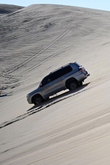 A silver SUV driving on a sandy road in a desert landscape. 3