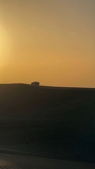 A vehicle on a desert dune during sunset. 1