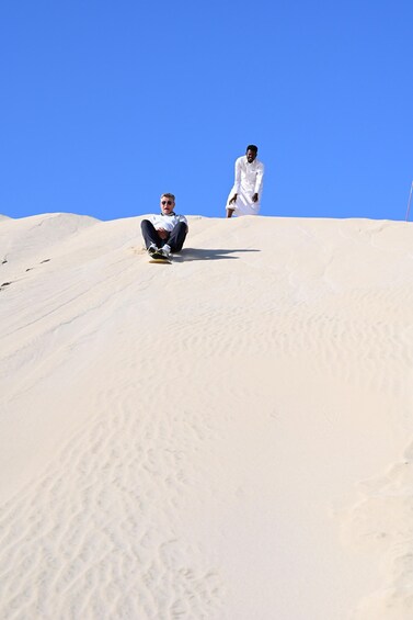 A person sliding down a sandy slope under a clear blue sky. 5