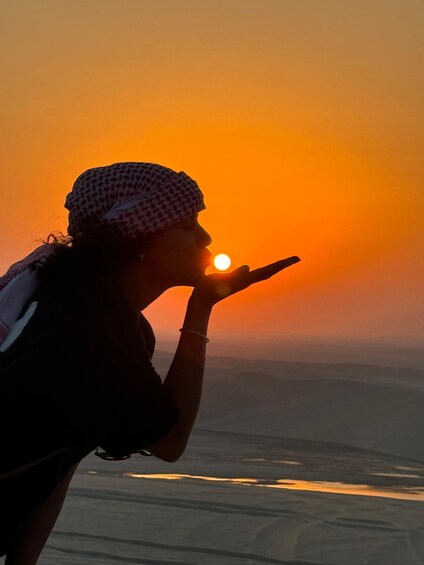 A person blowing a kiss towards the setting sun over a vast landscape. 4