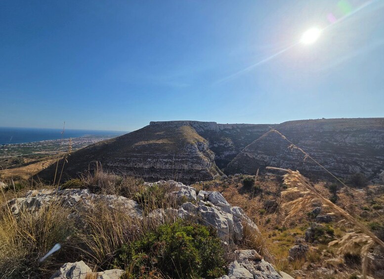 Un paisaje montañoso con un plateau destacado, terreno rocoso y una vista distante de un pueblo costero. 3