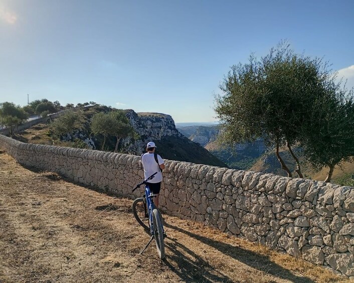 Una persona pedaleando en bicicleta junto a un muro de piedra, con vistas a un cañón. 5