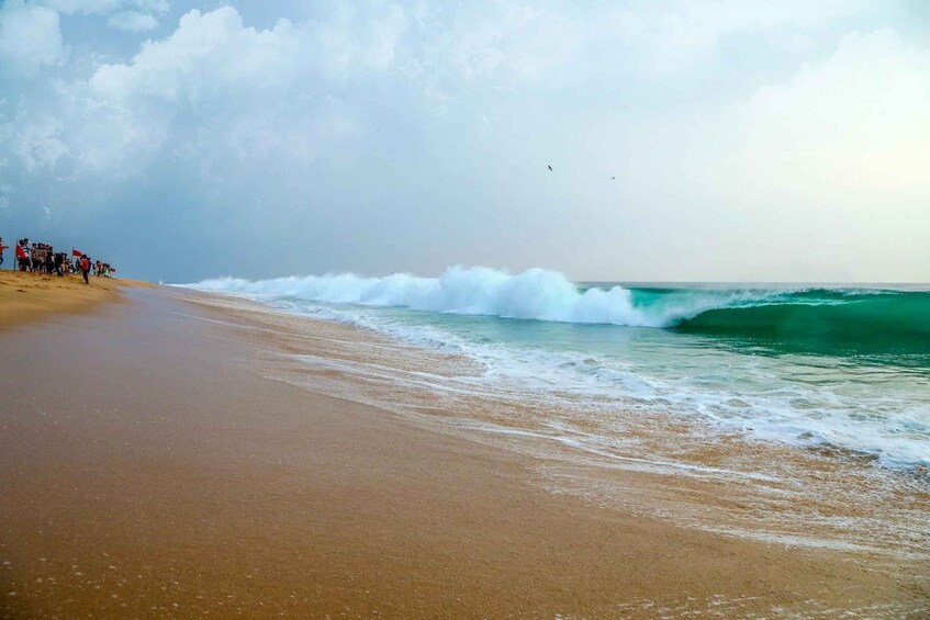 Una playa con olas, cielo nublado y un grupo de personas en la arena. 5