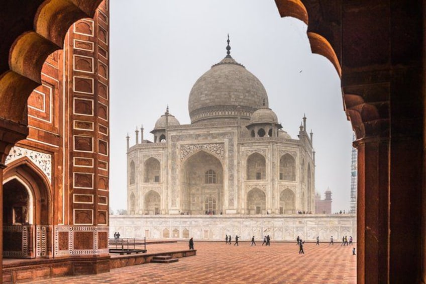 The Taj Mahal with a view through an archway, featuring intricate red and white marble work. 1