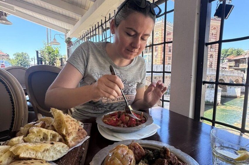 A person dining at a table with a bowl of food, a plate of bread, and a glass of water. 1
