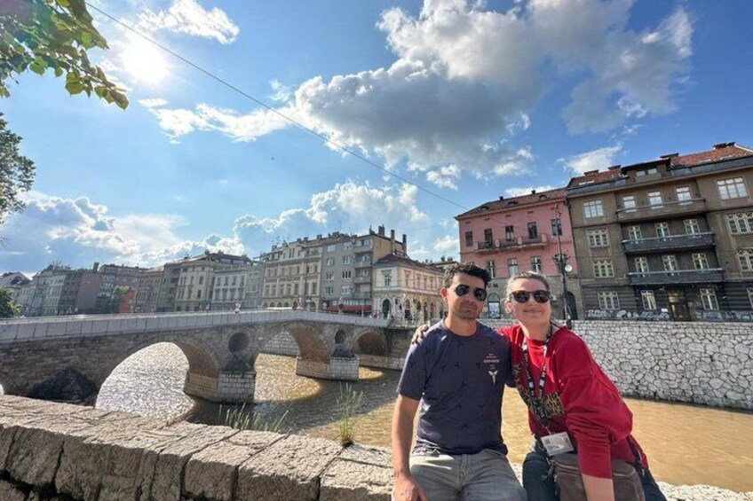 Two people standing by a stone bridge with buildings in the background. 5