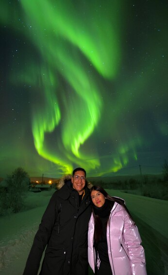 Two people standing in a snowy landscape with the Northern Lights in the background. 2