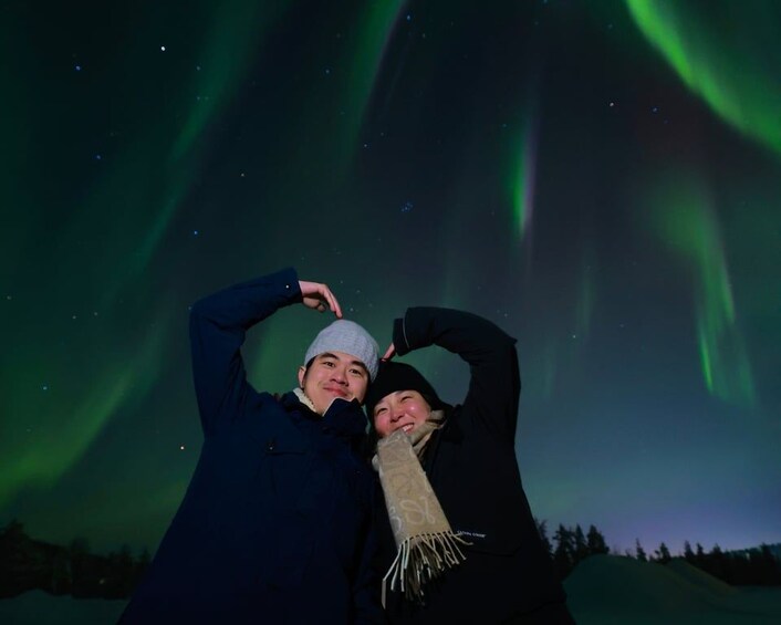 Two people posing with their arms raised against a night sky with green aurora borealis. 5