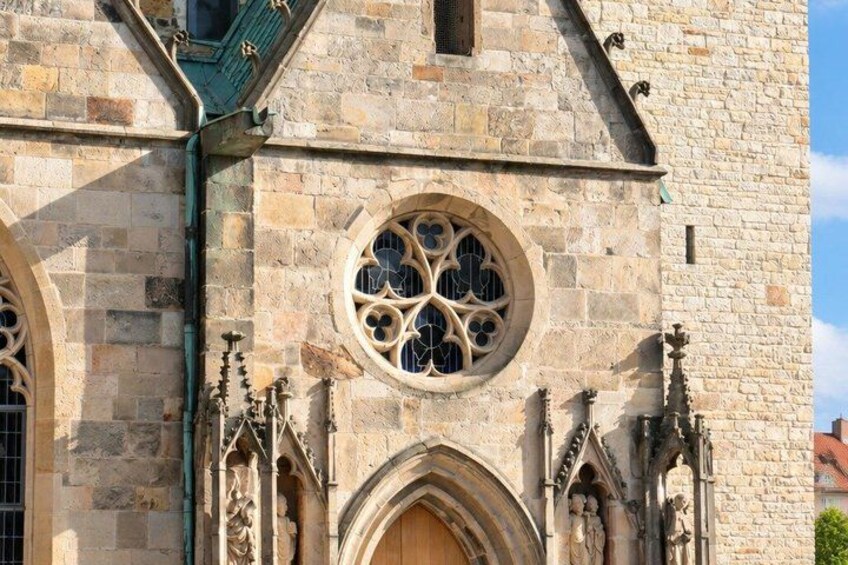 A stone building with a large circular window with intricate designs, a pointed arch doorway, and a small balcony with a green railing. 2