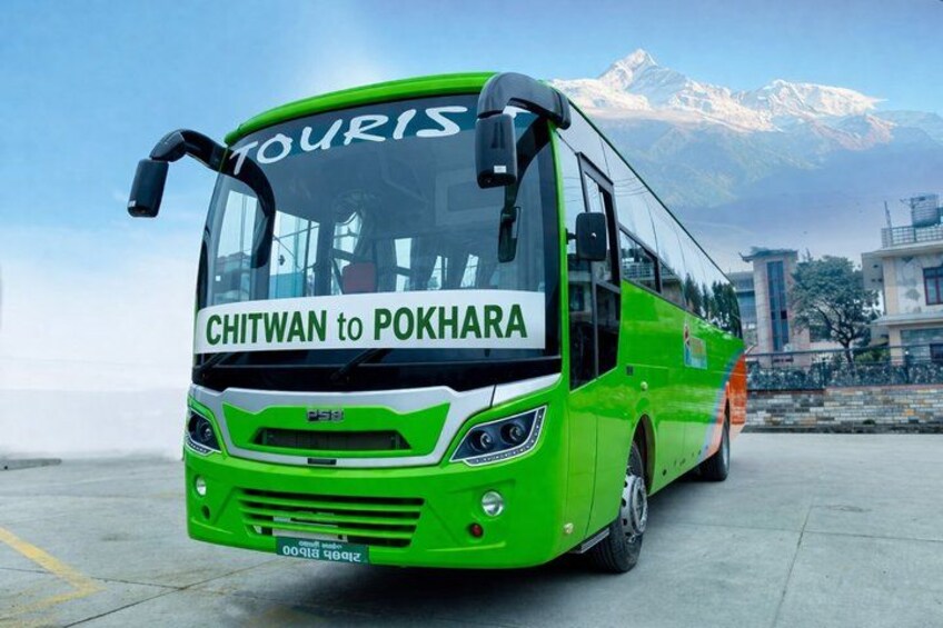 A green bus with 'CHITWAN to POKHARA' written on the front, parked on a road with mountains in the background. 4