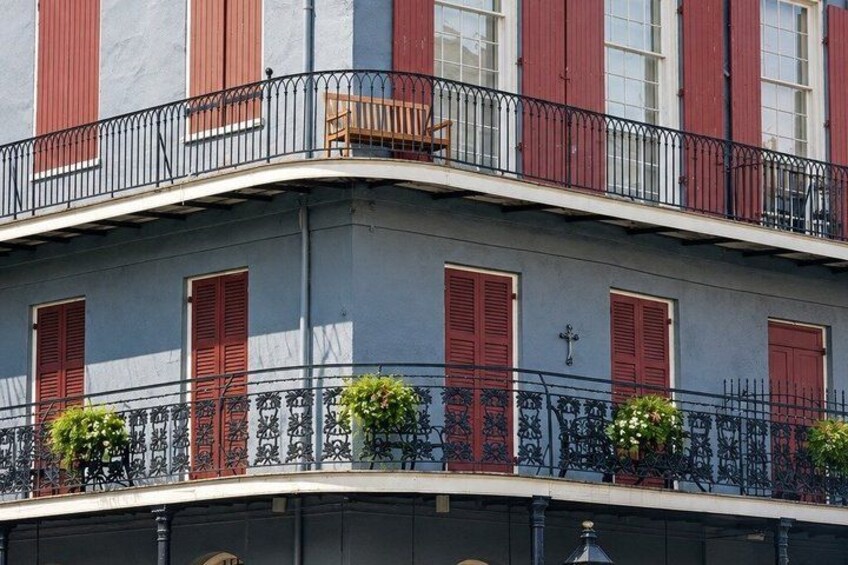 A building with red shutters, a balcony with a chair, and potted plants. 5
