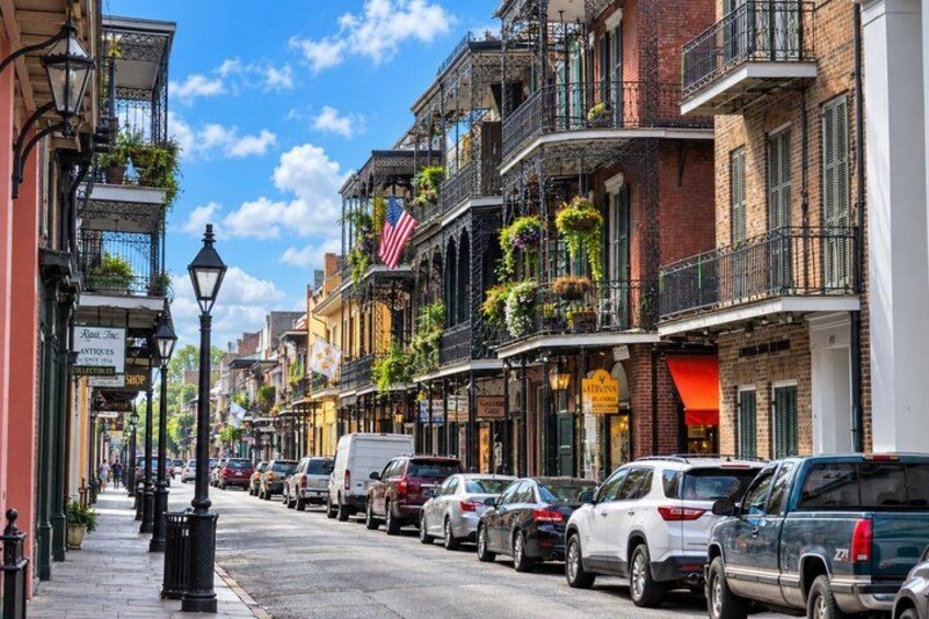 A street lined with multi-story buildings, parked cars, and hanging plants. 3