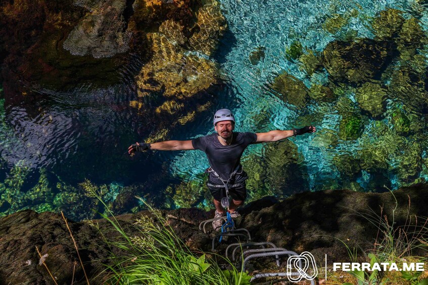 A person rappelling down a rocky cliff with clear blue water below. 1