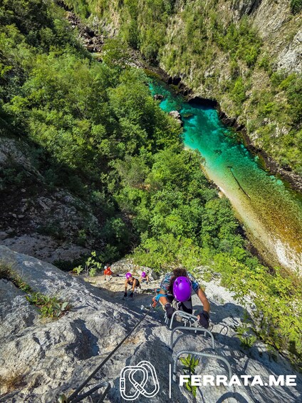 A person climbing a rocky path with a river and greenery in the background. 5