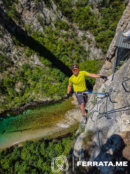 A person rappelling down a rocky cliff with a river below. 2