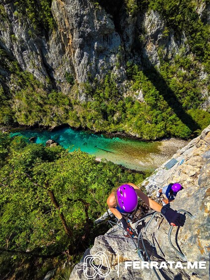 A person climbing a rocky cliff with a helmet and climbing gear, overlooking a turquoise river. 4