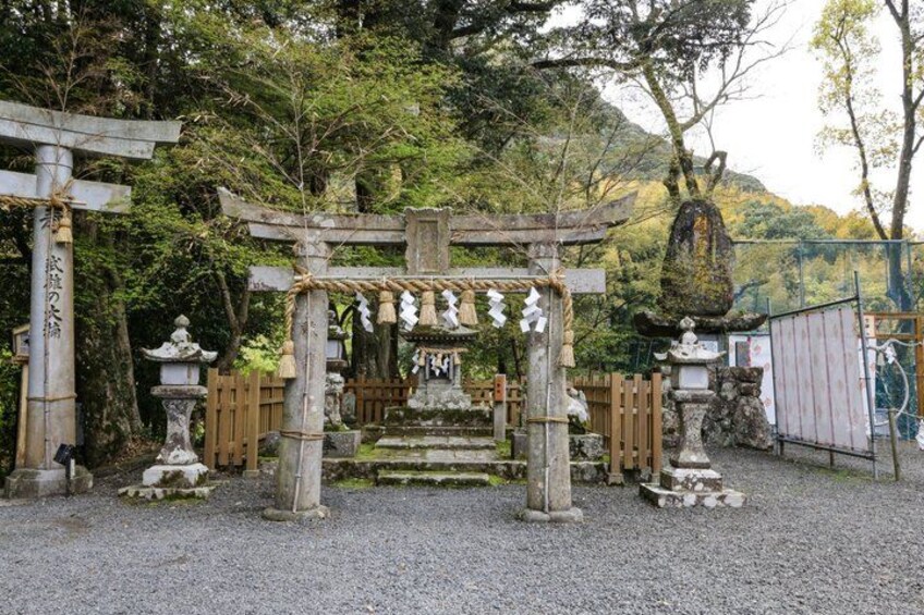 A traditional Japanese torii gate, stone lanterns, and a wooden fence in a forested area. 4