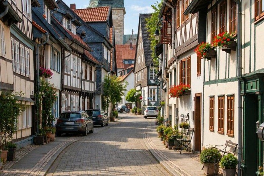 A cobblestone street lined with traditional half-timbered buildings, parked cars, and potted plants. 2