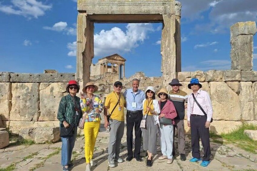 A group of people standing in front of ancient ruins with stone structures and a clear sky. 1