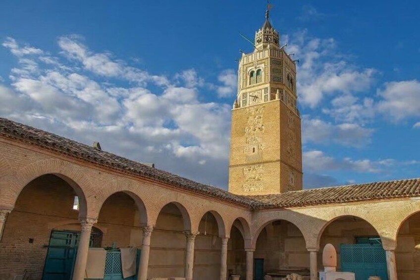 A historic building with a tall tower, arched walkways, and a clear sky. 3