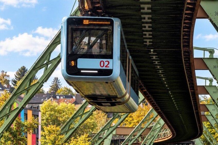 A tram with the number 02 on its display, passing under a bridge with green metal beams and a clear sky in the background. 3