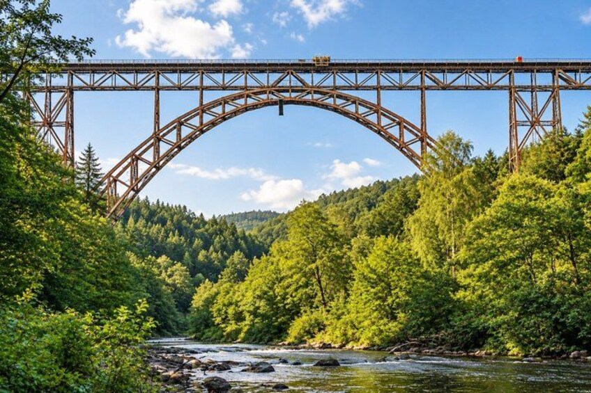 A steel bridge arching over a river, surrounded by dense green forest. 2