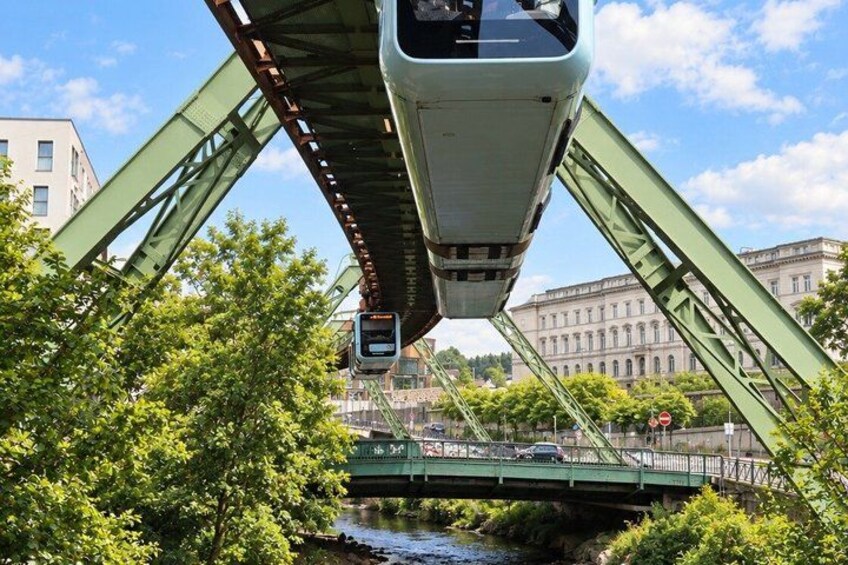 A green bridge with a train passing underneath. There are trees and buildings in the background. 4