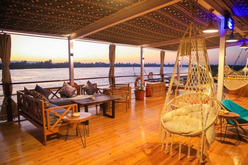 A wooden deck with outdoor furniture, a hanging chair, and a view of the water at sunset. 4